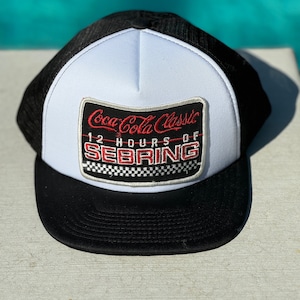 May include: Black and white trucker hat with a red and white Coca-Cola Classic 12 Hours of Sebring patch.