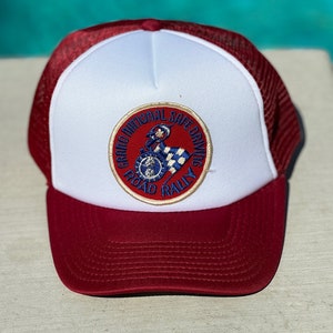 May include: A white and red trucker hat with a patch that says "Grand National Safe Driving Road Rally". The patch features a cartoon illustration of a person riding a motorcycle.
