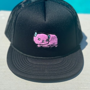 May include: A black mesh trucker hat with a pink cartoon cat embroidered on the front.