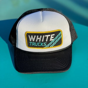 May include: A white and black trucker hat with a patch that says "WHITE TRUCKS" in yellow letters with a turquoise and white checkered pattern.