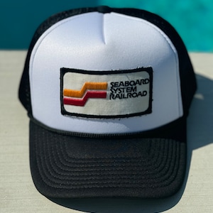May include: White and black trucker hat with a red, yellow, and orange logo that says "Seaboard System Railroad".