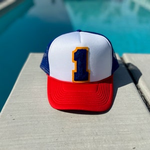May include: A red, white, and blue trucker hat with a large blue number "1" on the front. The number has a yellow outline.