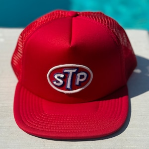 May include: Red trucker hat with a white mesh back and a blue and white embroidered STP logo.