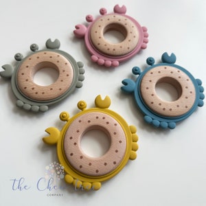 Puede incluir: Cuatro anillos de dentici&oacute;n de silicona con forma de cangrejo. Los anillos son de diferentes colores: rosa, verde, azul y amarillo. Cada anillo tiene un centro de madera con un patr&oacute;n de puntos.