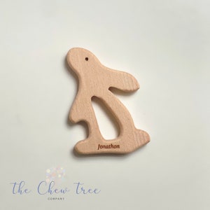 Puede incluir: Un mordedor de madera de color marrón claro en forma de conejo con el nombre "Jonathan" grabado en la parte inferior.