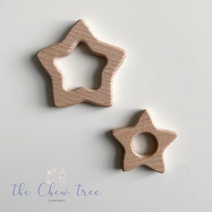 Op de afbeelding: Twee houten stervormige bijtringen. De grotere ster heeft een groter gat in het midden, terwijl de kleinere ster een kleiner gat heeft. Beide sterren zijn lichtbruin.