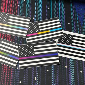 May include: Five black and white American flag stickers with different colored stripes. The stripes represent different causes and organizations.