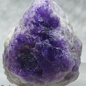 May include: A large, rough, purple and white color-change gemstone. The gemstone is a natural, raw, unpolished specimen.