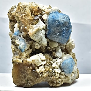 May include: A natural mineral specimen featuring a mix of colors and textures. The piece showcases a matrix of beige and white crystalline structures, with striking blue crystal formations. The overall appearance is rough and organic.