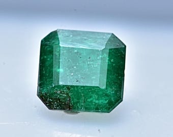 May include: A vibrant green emerald gemstone with a rectangular cut and a slightly cloudy appearance.