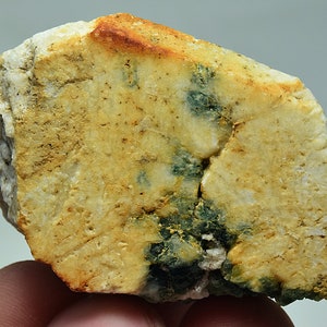 May include: A rough, light brown rock with green and yellow mineral inclusions.