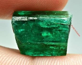 Può includere: Un cristallo di smeraldo verde vibrante con un'inclusione di pirite visibile. Il cristallo è sfaccettato e ha una forma rettangolare.