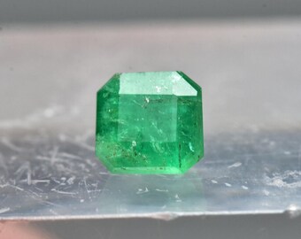 May include: A vibrant green emerald gemstone with a rectangular cut and a slightly cloudy appearance.