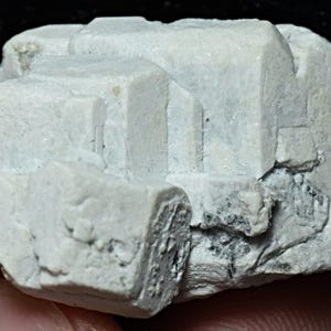 May include: A cluster of white, opaque, cubic crystals with a rough, textured surface. The crystals are clustered together in a random, organic pattern.