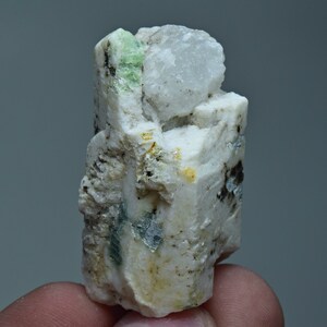 May include: A white and green crystal cluster with a large, clear crystal on top. The crystal cluster is rough and has a natural, earthy look.