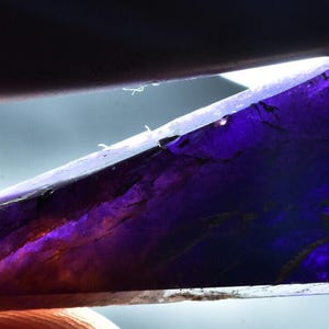 Puede incluir: Una piedra preciosa de cambio de color púrpura y azul con un corte facetado. La piedra preciosa se sostiene en una mano.