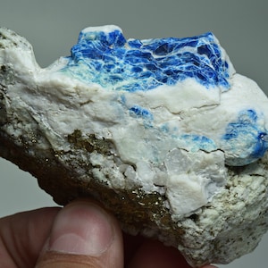 May include: A rough, gray rock with a blue and white mineral deposit. The mineral has a layered, striated appearance.