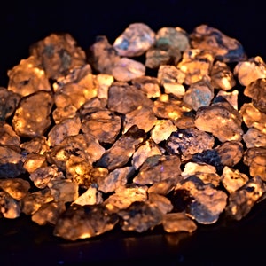 May include: A close-up of a pile of translucent, light blue and gray stones. The stones are illuminated from below, creating a warm, orange glow.