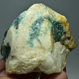 May include: A rough, white rock with green and yellow mineral inclusions. The rock has a natural, unpolished surface.