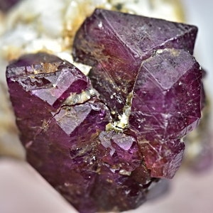 May include: A cluster of deep red ruby crystals with a faceted, geometric shape. The crystals are intergrown and have a slightly rough texture.