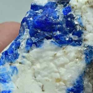 May include: A close-up of a blue and white mineral specimen. The mineral has a rough, textured surface and is composed of small, blue crystals embedded in a white matrix.