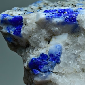 Op de afbeelding: Een close-up van een ruwe, witte rots met ingebedde blauwe kristallen. De kristallen zijn scherp en hoekig, met een diepblauwe kleur.