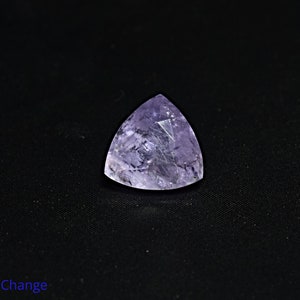 May include: A triangular, faceted gemstone with a purple hue. The gemstone is set against a black background. Color Change.