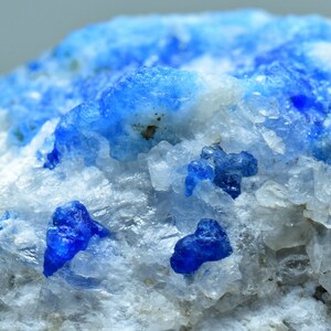 May include: Close-up of a rock formation with small, bright blue crystals embedded in a white, crystalline matrix.