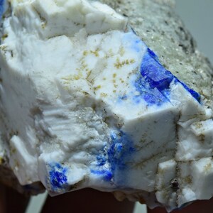 May include: A close-up of a white mineral specimen with blue accents. The mineral has a rough, crystalline texture.