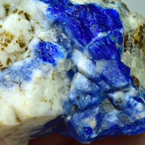 Op de afbeelding: Een ruw, natuurlijk exemplaar van blauwe en witte lapis lazuli. De steen heeft verschillende texturen en tinten blauw.