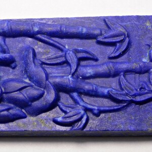 May include: A rectangular, deep blue stone carving featuring a bamboo design. The relief carving shows bamboo stalks and leaves, with a textured surface and subtle gold flecks. The overall theme is nature and artistry.