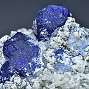May include: A cluster of deep blue lapis lazuli crystals embedded in a matrix of white calcite and pyrite. The crystals have a rough, natural texture and a deep, rich blue color.