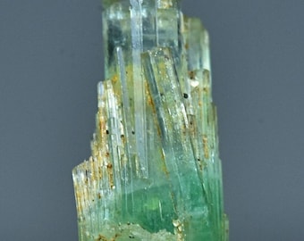 Puede incluir: Un grupo de cristales de berilo verde, también conocidos como esmeraldas, con una apariencia vítrea y translúcida. Los cristales son alargados y tienen una superficie estriada.