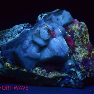 Könnte beinhalten: Nahaufnahme einer Gesteinsformation unter einer kurzwelligen UV-Lampe. Der Stein ist hellblau mit einigen roten und gelben Akzenten. Der Text "SHORT WAVE" ist am unteren Rand des Bildes sichtbar.