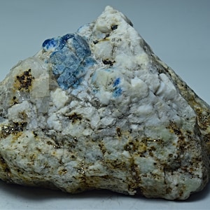 May include: A rough, gray rock with a cluster of blue and white crystals. The rock has a speckled appearance with small, gold-colored flecks.