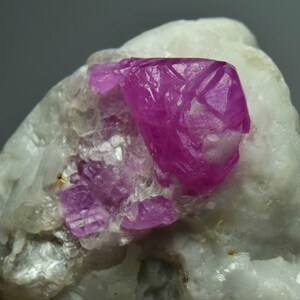 以下が含まれることがあります： 白いマトリックスに埋め込まれた鮮やかなピンクのルビーの結晶。ルビーは鋭くファセットカットされており、光沢のある仕上がりです。