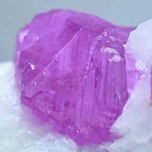 May include: A vibrant, purple, faceted crystal with a sharp, geometric shape. The crystal is set against a white background.