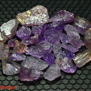 May include: A collection of rough amethyst crystals in various shades of purple. The crystals are translucent and have a natural, unpolished appearance.