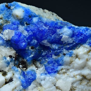 May include: A close-up of a blue mineral specimen with white and gray matrix. The blue mineral crystals are clustered together and have a shiny, metallic luster.
