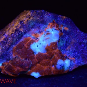 May include: A close-up of a rock with a variety of colors, including blue, purple, orange, and white. The rock is illuminated with a long wave UV light, causing it to fluoresce.