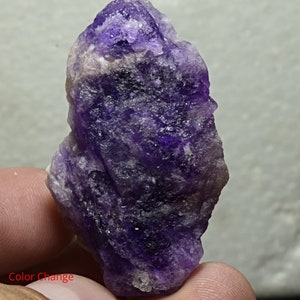 May include: A purple amethyst crystal with a rough, textured surface. The crystal has a deep purple color with some lighter areas. The crystal is about 2 inches tall and 1 inch wide.