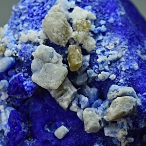 May include: A close-up of a blue mineral specimen with white and green crystals. The blue mineral is a deep, rich blue color, and the crystals are scattered across the surface.