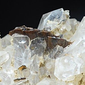 Puede incluir: Un grupo de cristales de cuarzo transparentes con una inclusión mineral marrón. Los cristales son afilados y bien formados, con un brillo vítreo.