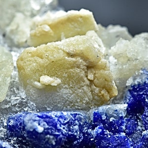 May include: Close-up of a cluster of white and yellow crystals with a blue mineral in the background.