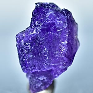 May include: A deep purple amethyst crystal with a rough, faceted surface. The crystal is translucent and has a slight sheen.