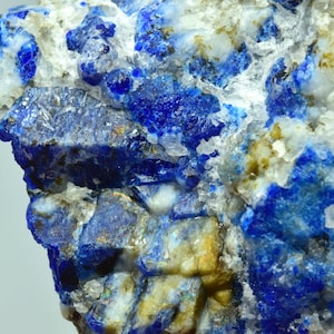 Op de afbeelding: Een close-up van een blauw en wit mineraalmonster. Het mineraal heeft een ruw, getextureerd oppervlak en is samengesteld uit kleine, kristallijne structuren. De blauwe kristallen zijn doorspekt met witte kristallen, wat een opvallend contrast creëert.