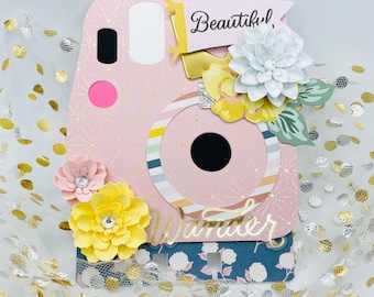 Könnte beinhalten: Eine rosa und weiße Papierbastelkamera mit einem Objektiv, einer weißen Blume und einer gelben Blume. Die Kamera trägt die Worte "Beautiful" und "Wander".
