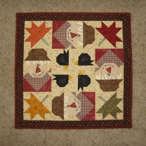 Pode incluir: Uma tapeçaria de parede quadrada acolchoada com desenhos temáticos de outono. A colcha apresenta espantalhos, pássaros pretos e folhas de outono em várias cores, incluindo vermelho, laranja e castanho. A borda é vermelha escura com pequenas bolinhas coloridas.