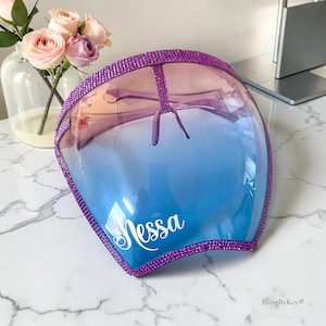 May include: A full-face protective visor featuring a gradient transition from pink at the top to blue at the bottom. The edges are lined with purple rhinestones, and the name Nessa is printed in white script on the lower left side of the visor.