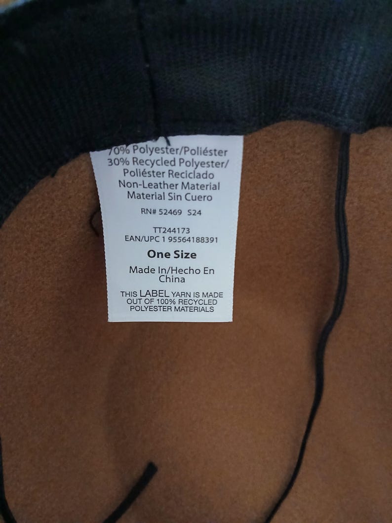 May include: A close-up of a hat's interior, featuring a brown fabric and a black brim. A white label displays text including "70% Polyester", "One Size", and "Made In China". The label also states the yarn is made of 100% recycled polyester materials.